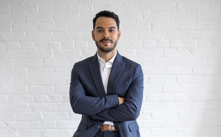 Brandon Solomon standing in a suit against a white brick wall